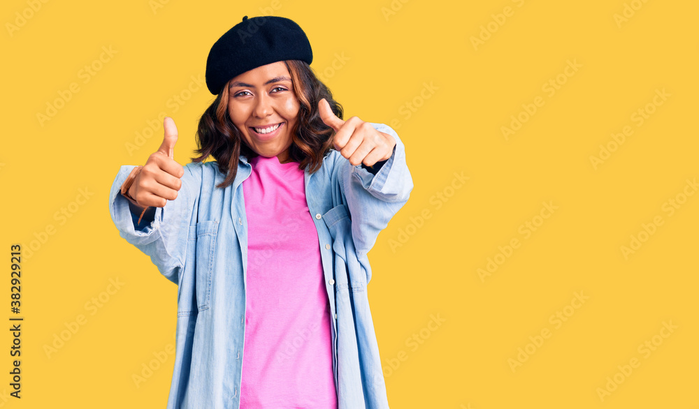 Young beautiful mixed race woman wearing french look with beret approving doing positive gesture with hand, thumbs up smiling and happy for success. winner gesture. Young beautiful mixed race woman wearing french look with beret approving doing positive gesture with hand, thumbs up smiling and happy for success. winner gesture.