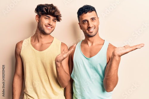 Young gay couple wearing casual clothes smiling cheerful presenting and pointing with palm of hand looking at the camera.