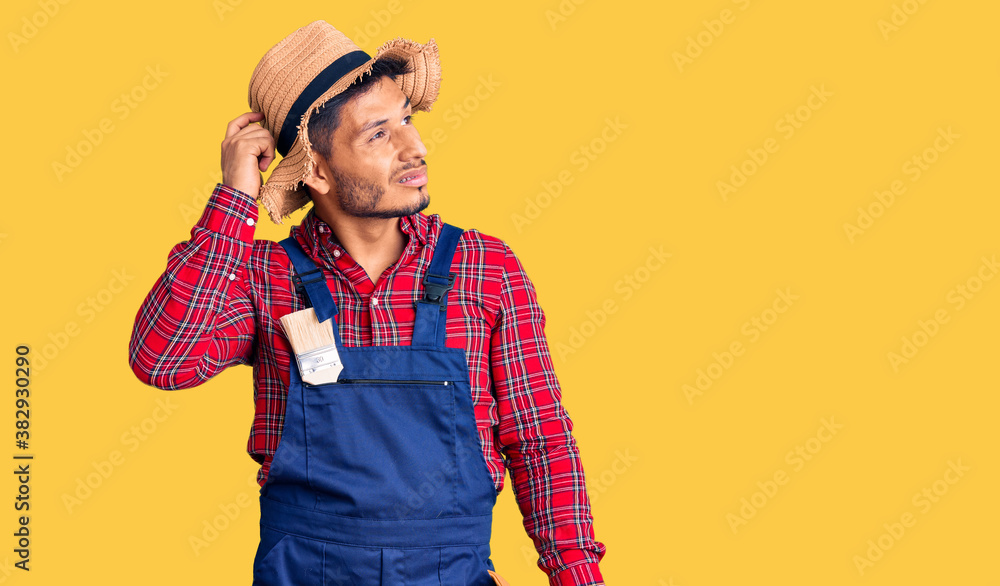 Handsome latin american young man weaing handyman uniform confuse and wondering about question. uncertain with doubt, thinking with hand on head. pensive concept. Handsome latin american young man weaing handyman uniform confuse and wondering about question. uncertain with doubt, thinking with hand on head. pensive concept.