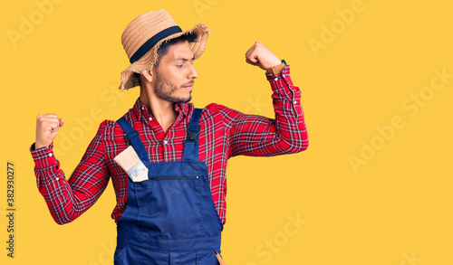 Handsome latin american young man weaing handyman uniform showing arms muscles smiling proud. fitness concept.