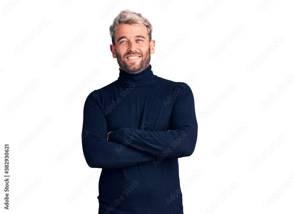 Young handsome blond man wearing casual turtleneck sweater happy face smiling with crossed arms looking at the camera. positive person. Young handsome blond man wearing casual turtleneck sweater happy face smiling with crossed arms looking at the camera. positive person.