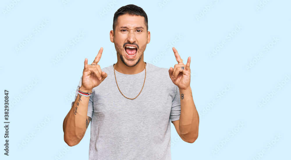 Handsome man with tattoos wearing 90s style shouting with crazy expression doing rock symbol with hands up. music star. heavy concept. Handsome man with tattoos wearing 90s style shouting with crazy expression doing rock symbol with hands up. music star. heavy concept.