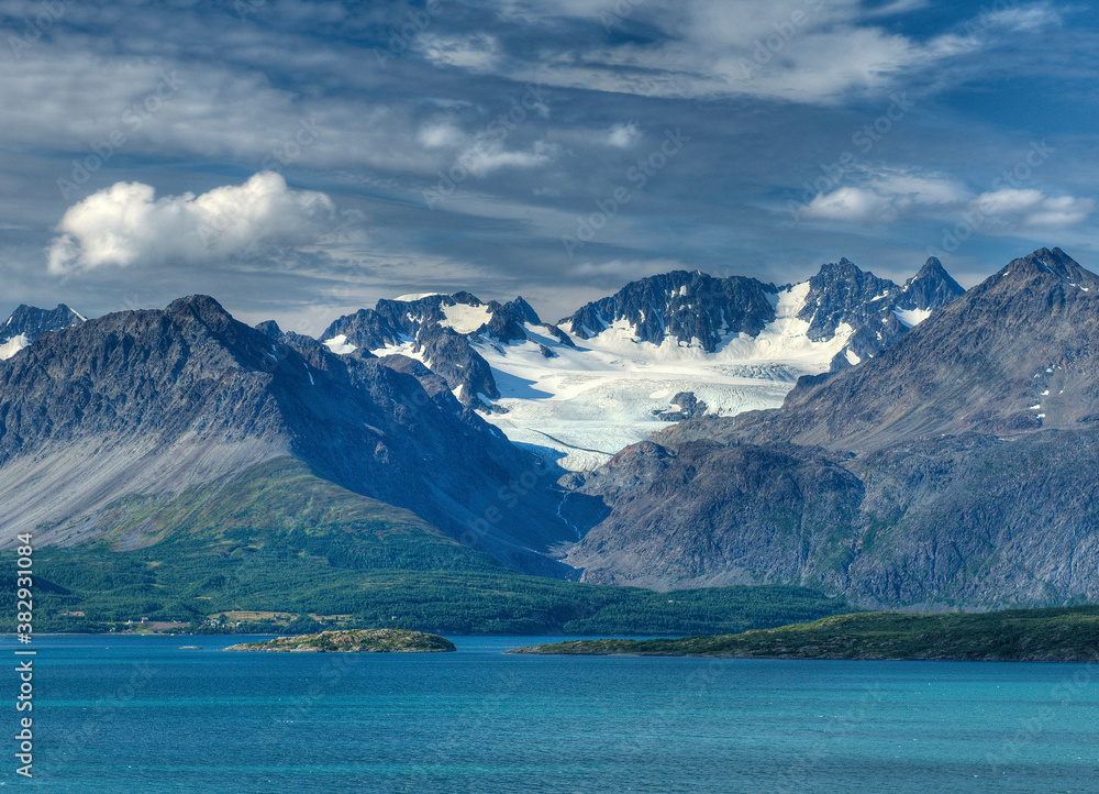 View To The Glacier Covered Lyngen Alps Mountains At Lyngenfjord On A Sunny Summer Day With A Clear Blue Sky And A Few Clouds