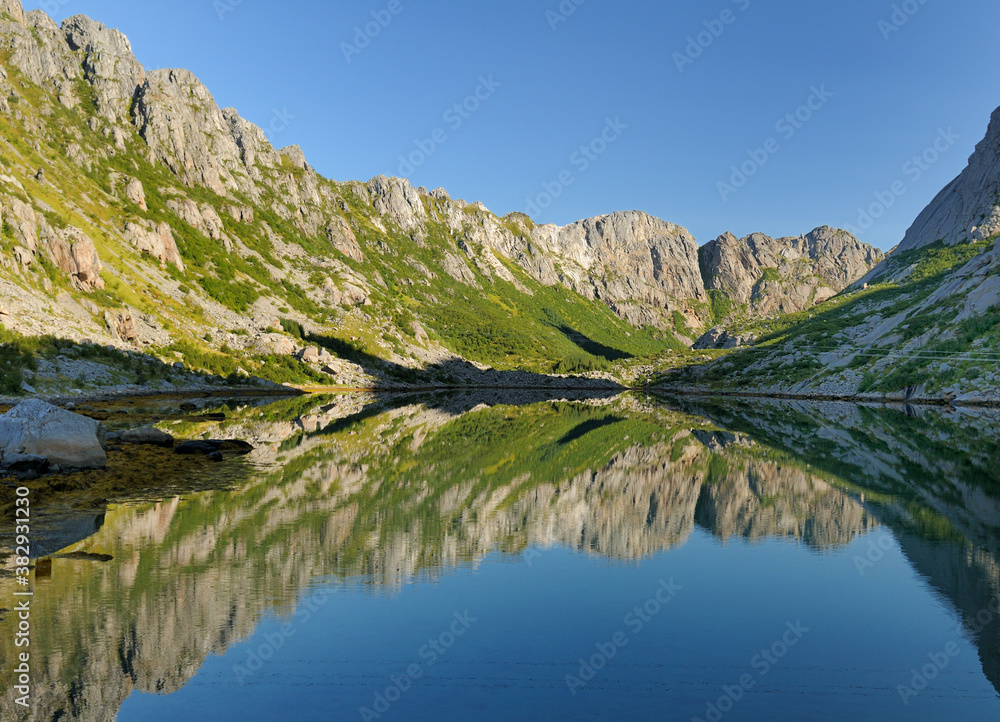 Mountains Reflecting In The Water On Lofoten Island Austvagoy On A Sunny Summer Day With A Clear Blue Sky