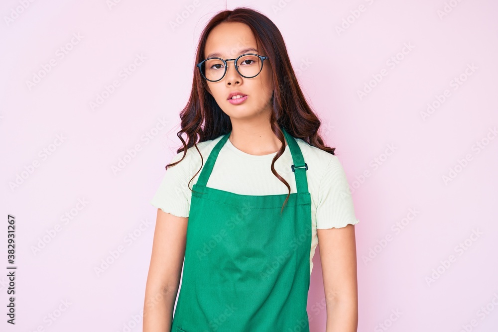 Young beautiful chinese girl wearing cleaner apron relaxed with serious expression on face. simple and natural looking at the camera. Young beautiful chinese girl wearing cleaner apron relaxed with serious expression on face. simple and natural looking at the camera.