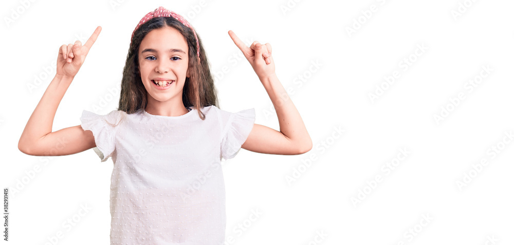 Cute hispanic child girl wearing casual white tshirt smiling amazed and surprised and pointing up with fingers and raised arms. Cute hispanic child girl wearing casual white tshirt smiling amazed and surprised and pointing up with fingers and raised arms.