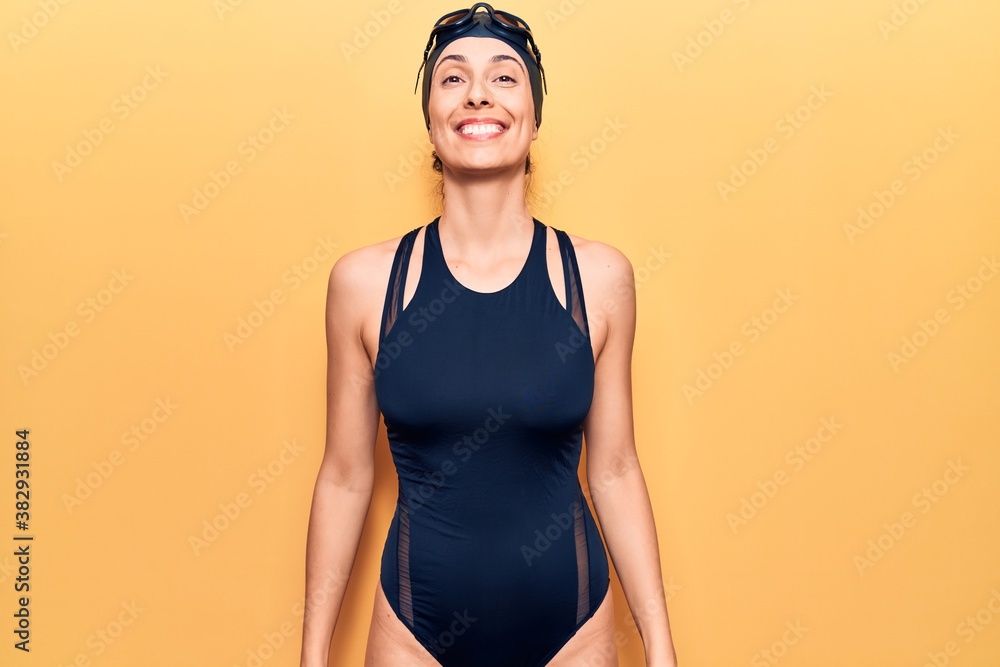 Young beautiful hispanic woman wearing swimwear and swimmer glasses looking positive and happy standing and smiling with a confident smile showing teeth Young beautiful hispanic woman wearing swimwear and swimmer glasses looking positive and happy standing and smiling with a confident smile showing teeth