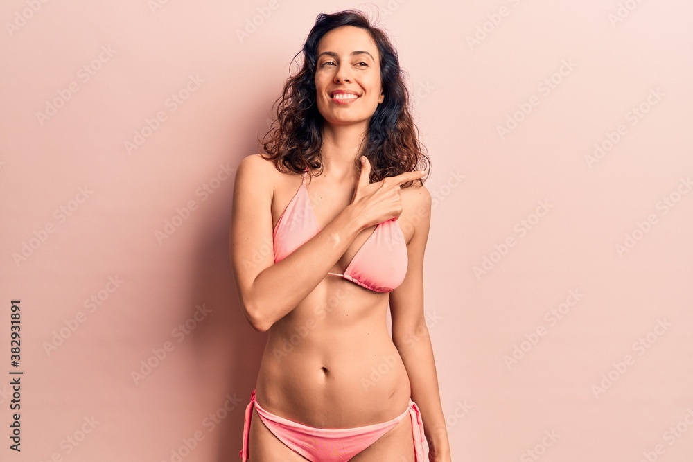 Young beautiful hispanic woman wearing bikini smiling cheerful pointing with hand and finger up to the side Young beautiful hispanic woman wearing bikini smiling cheerful pointing with hand and finger up to the side