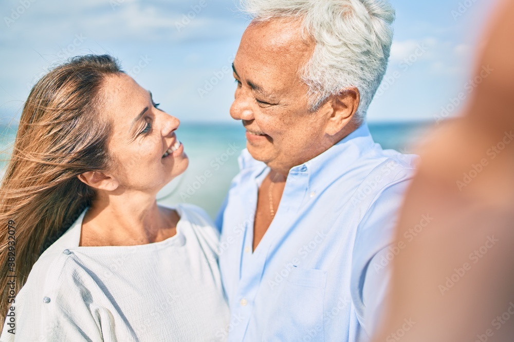 Middle age hispanic couple smiling happy making selfie by the camera at the beach. Middle age hispanic couple smiling happy making selfie by the camera at the beach.
