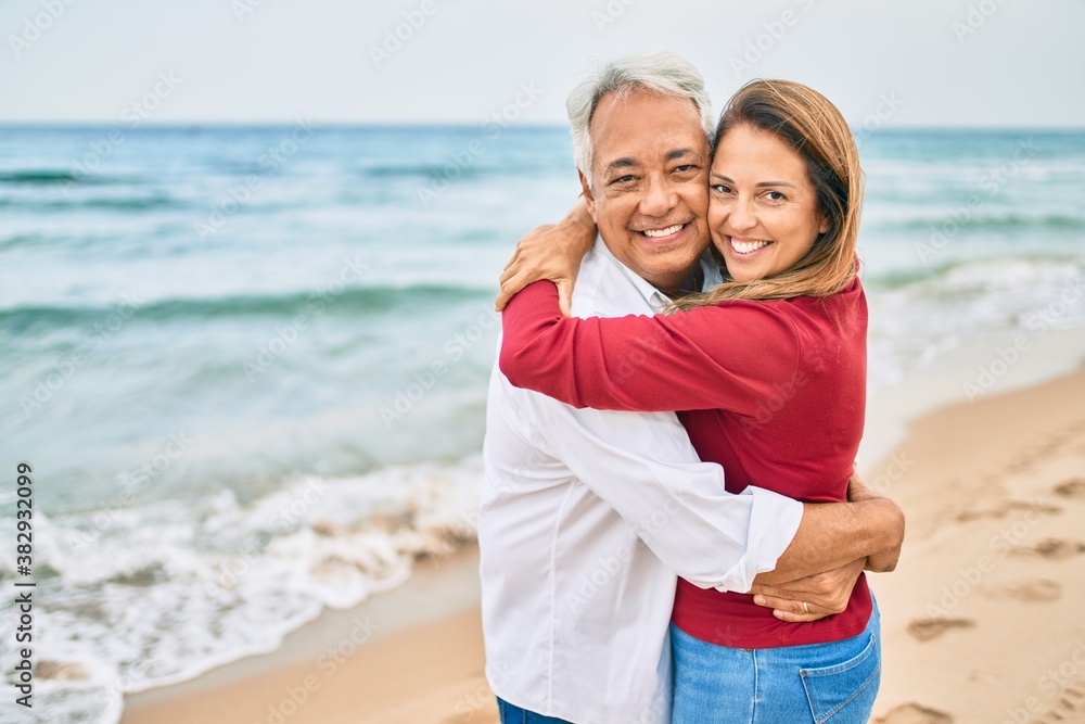 Middle age hispanic couple smiling happy and hugging walking at the beach Middle age hispanic couple smiling happy and hugging walking at the beach