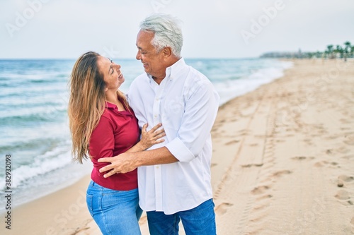Middle age hispanic couple smiling happy and hugging walking at the beach