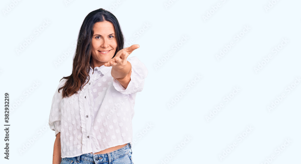 Young beautiful brunette woman wearing casual shirt smiling friendly offering handshake as greeting and welcoming. successful business. Young beautiful brunette woman wearing casual shirt smiling friendly offering handshake as greeting and welcoming. successful business.