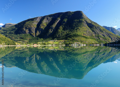 Mountains Reflecting In The Calm Water Of The Dalsfjord Near Skjolden On A Sunny Summer Day With A Clear Blue Sky And A Few Clouds