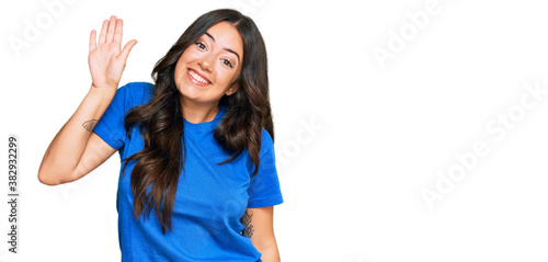 Beautiful brunette young woman wearing casual clothes waiving saying hello happy and smiling, friendly welcome gesture