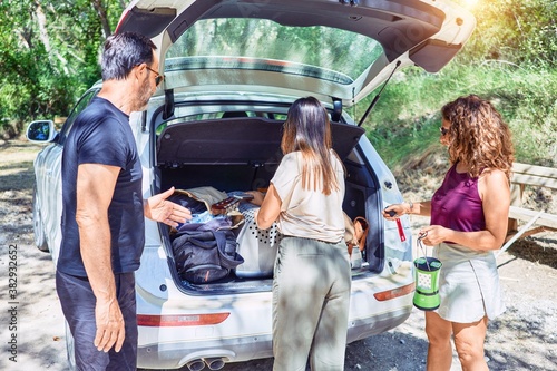 Family holding suitcase and backpack to the car trunk at forest
