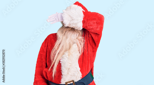 Old senior man with grey hair and long beard wearing traditional santa claus costume covering eyes with arm smiling cheerful and funny. blind concept.