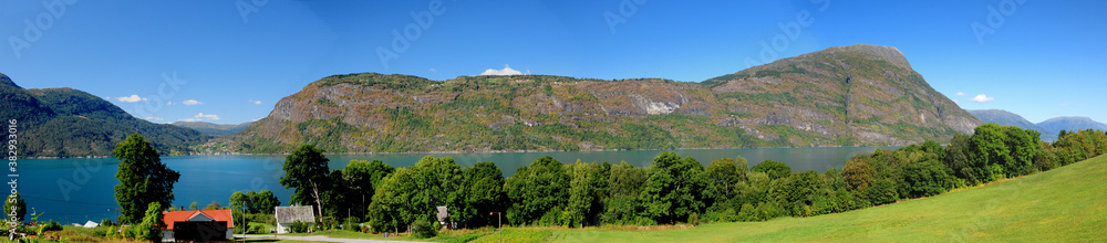 Panorama View Of The Mountains And The Calm Water Of The Dalsfjord Near Skjolden On A Sunny Summer Day With A Clear Blue Sky And A Few Clouds