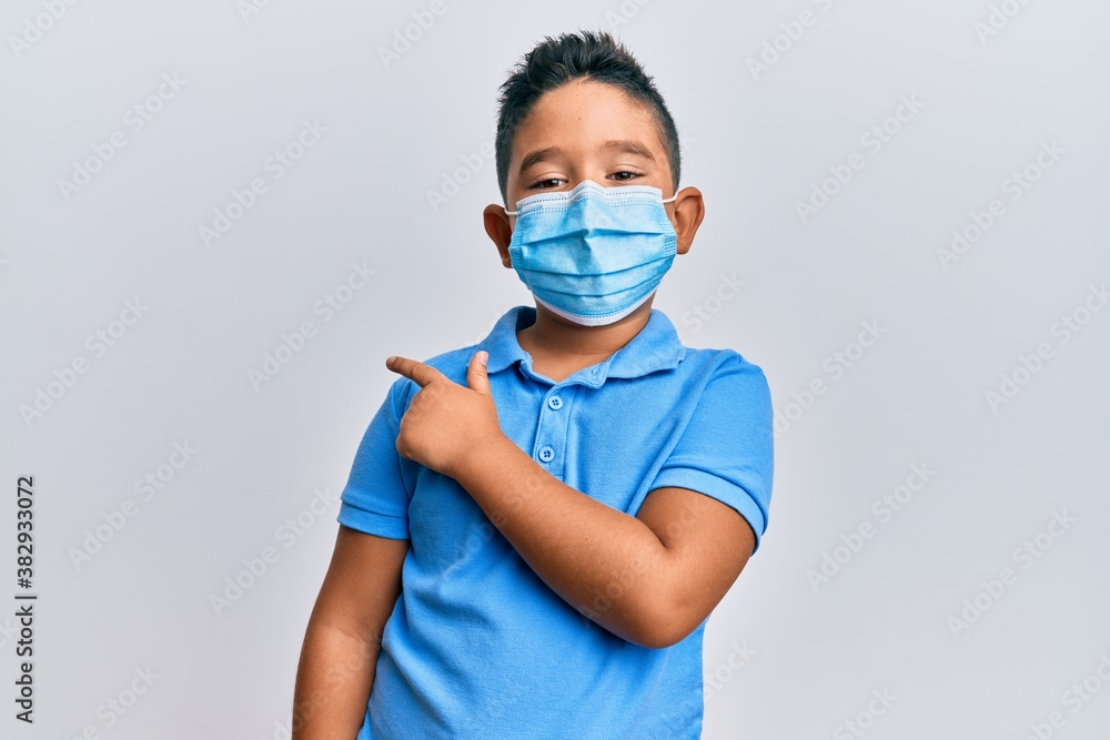 Little boy hispanic kid wearing medical mask smiling cheerful pointing with hand and finger up to the side Little boy hispanic kid wearing medical mask smiling cheerful pointing with hand and finger up to the side
