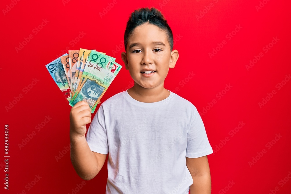 Little boy hispanic kid holding australian dollars looking positive and happy standing and smiling with a confident smile showing teeth Little boy hispanic kid holding australian dollars looking positive and happy standing and smiling with a confident smile showing teeth