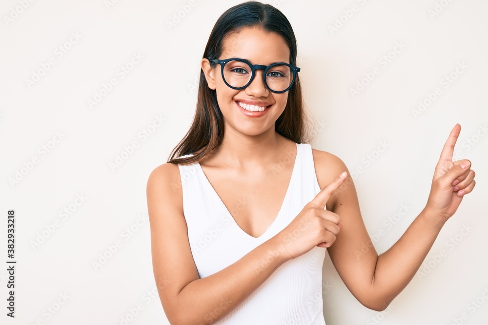 Young beautiful latin girl wearing casual clothes and glasses smiling and looking at the camera pointing with two hands and fingers to the side. Young beautiful latin girl wearing casual clothes and glasses smiling and looking at the camera pointing with two hands and fingers to the side.