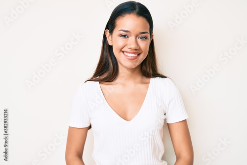 Young beautiful latin girl wearing casual white tshirt with a happy and cool smile on face. lucky person.
