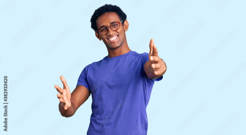 African handsome man wearing casual clothes and glasses looking at the camera smiling with open arms for hug. cheerful expression embracing happiness. African handsome man wearing casual clothes and glasses looking at the camera smiling with open arms for hug. cheerful expression embracing happiness.
