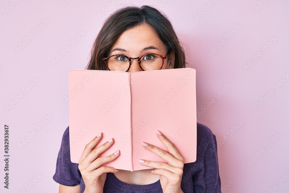 Young beautiful woman wearing glasses reading book celebrating crazy and amazed for success with open eyes screaming excited. Young beautiful woman wearing glasses reading book celebrating crazy and amazed for success with open eyes screaming excited.