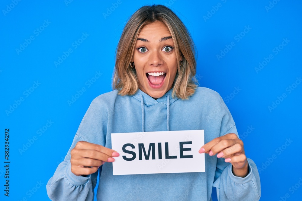 Beautiful caucasian woman holding smile text celebrating crazy and amazed for success with open eyes screaming excited. Beautiful caucasian woman holding smile text celebrating crazy and amazed for success with open eyes screaming excited.
