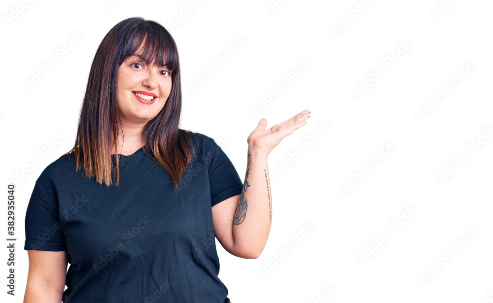 Young plus size woman wearing casual clothes smiling cheerful presenting and pointing with palm of hand looking at the camera. Young plus size woman wearing casual clothes smiling cheerful presenting and pointing with palm of hand looking at the camera.
