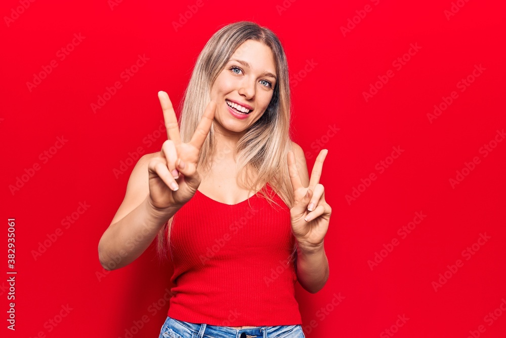 Young blonde woman wearing casual clothes smiling looking to the camera showing fingers doing victory sign. number two. Young blonde woman wearing casual clothes smiling looking to the camera showing fingers doing victory sign. number two.