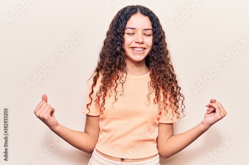 Beautiful kid girl with curly hair wearing casual clothes very happy and excited doing winner gesture with arms raised, smiling and screaming for success. celebration concept. © Krakenimages.com
