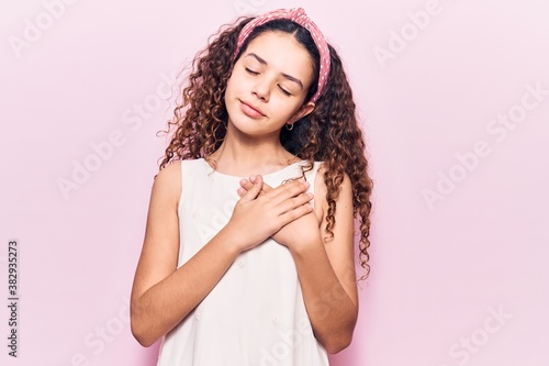 Beautiful kid girl with curly hair wearing casual clothes smiling with hands on chest with closed eyes and grateful gesture on face. health concept.