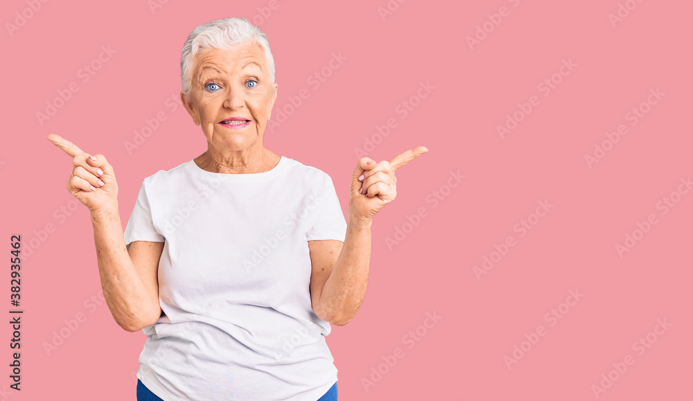 Senior beautiful woman with blue eyes and grey hair wearing casual white tshirt smiling confident pointing with fingers to different directions. copy space for advertisement Senior beautiful woman with blue eyes and grey hair wearing casual white tshirt smiling confident pointing with fingers to different directions. copy space for advertisement