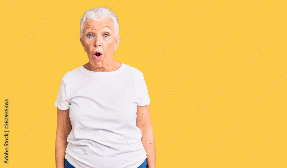 Senior beautiful woman with blue eyes and grey hair wearing casual white tshirt in shock face, looking skeptical and sarcastic, surprised with open mouth Senior beautiful woman with blue eyes and grey hair wearing casual white tshirt in shock face, looking skeptical and sarcastic, surprised with open mouth