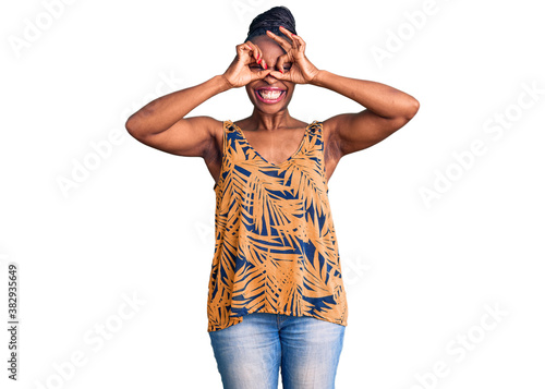 Young african american woman wearing casual clothes doing ok gesture like binoculars sticking tongue out, eyes looking through fingers. crazy expression. © Krakenimages.com