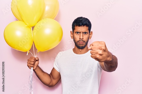 Young latin man holding balloons annoyed and frustrated shouting with anger, yelling crazy with anger and hand raised © Krakenimages.com