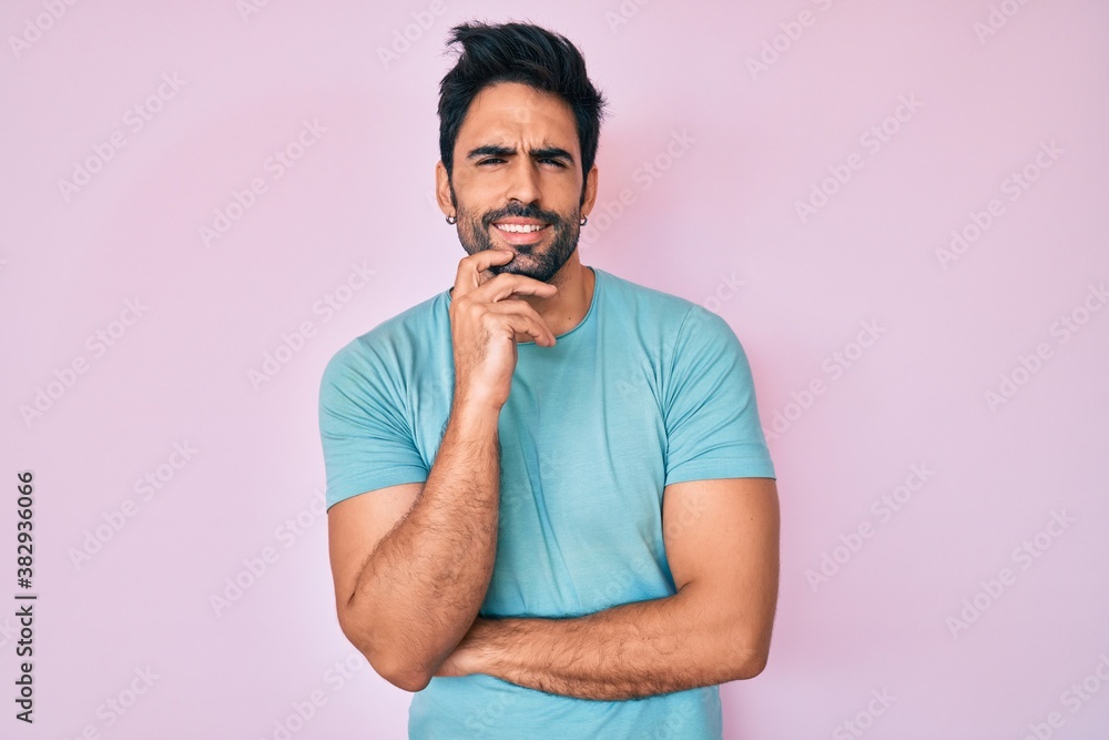 Obraz premium Handsome hispanic man with beard wearing casual clothes looking confident at the camera with smile with crossed arms and hand raised on chin. thinking positive.