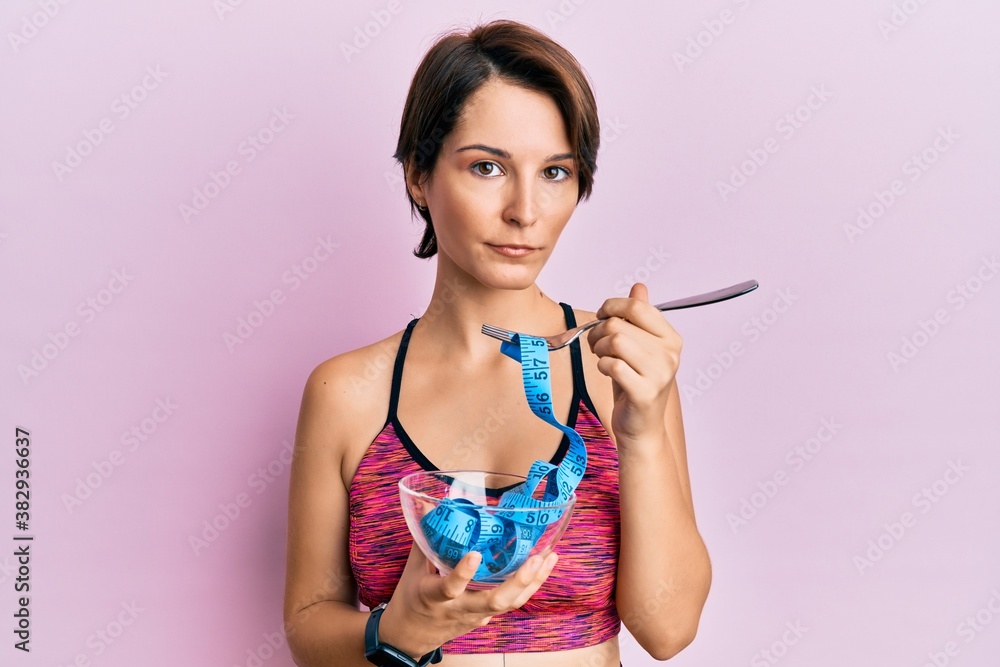 Young brunette woman with short hair eating measure meter doing diet for weight loss relaxed with serious expression on face. simple and natural looking at the camera. Young brunette woman with short hair eating measure meter doing diet for weight loss relaxed with serious expression on face. simple and natural looking at the camera.
