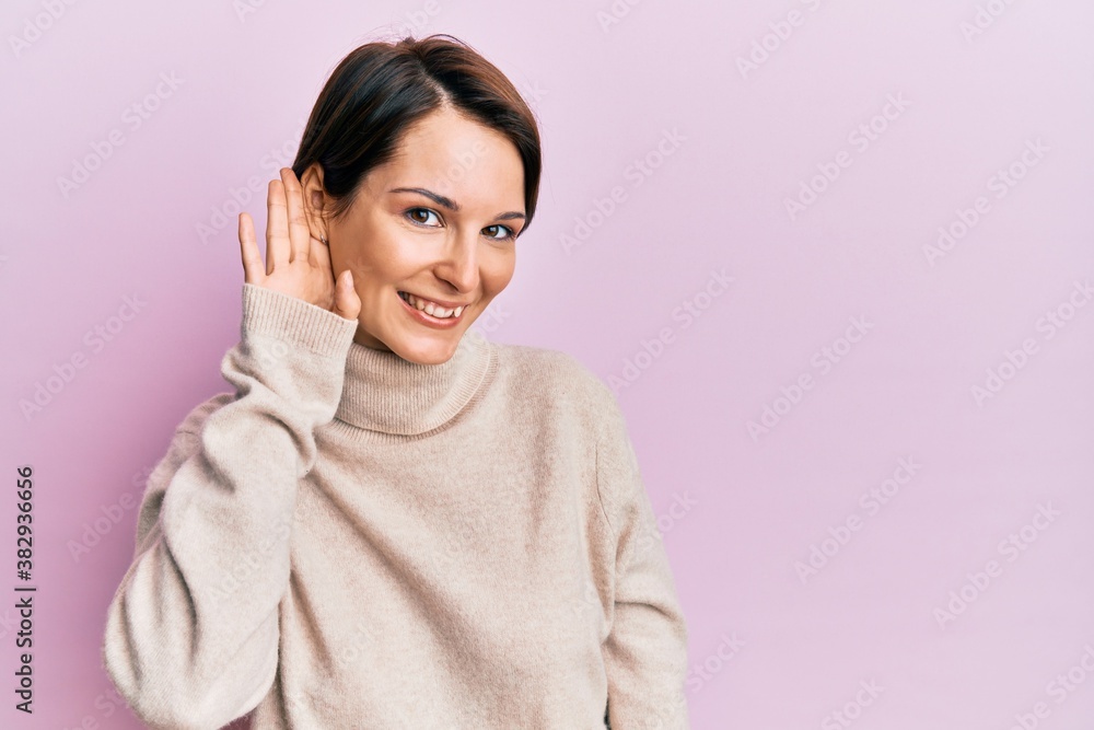 Young brunette woman with short hair wearing casual winter sweater smiling with hand over ear listening an hearing to rumor or gossip. deafness concept. Young brunette woman with short hair wearing casual winter sweater smiling with hand over ear listening an hearing to rumor or gossip. deafness concept.