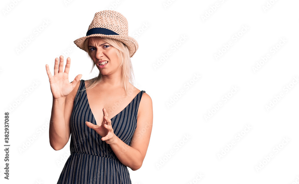 Young beautiful blonde woman wearing summer hat and dress disgusted expression, displeased and fearful doing disgust face because aversion reaction. with hands raised Young beautiful blonde woman wearing summer hat and dress disgusted expression, displeased and fearful doing disgust face because aversion reaction. with hands raised
