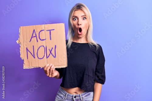 Young beautiful blonde woman asking for social reaction holding banner with act now message scared and amazed with open mouth for surprise, disbelief face