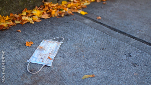 Blue Disposable Face Mask Discarded on Sidewalk by a Pile of Autumn Leaves
