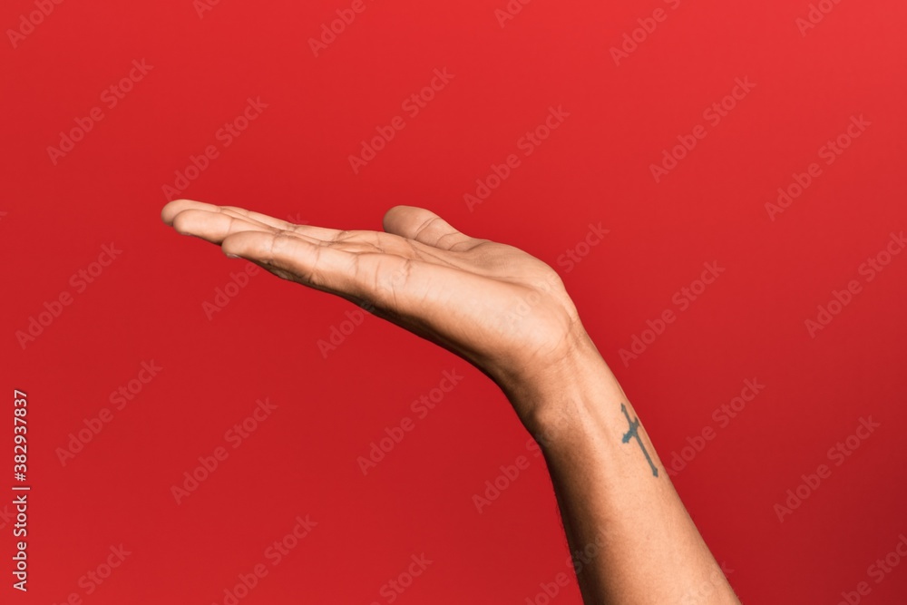 Hand of hispanic man over red isolated background with flat palm presenting product, offer and giving gesture, blank copy space
