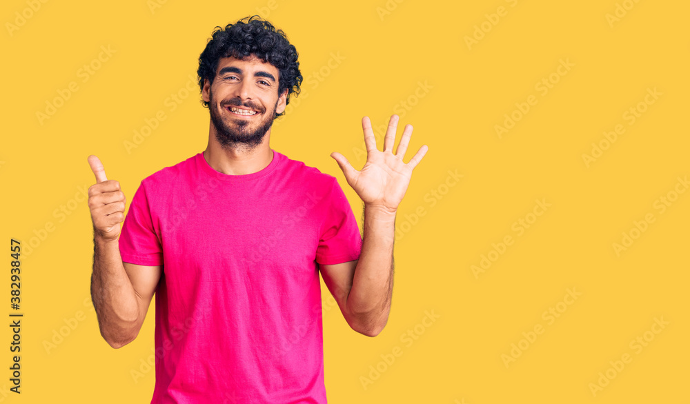 Handsome young man with curly hair and bear wearing casual pink tshirt showing and pointing up with fingers number six while smiling confident and happy. Handsome young man with curly hair and bear wearing casual pink tshirt showing and pointing up with fingers number six while smiling confident and happy.