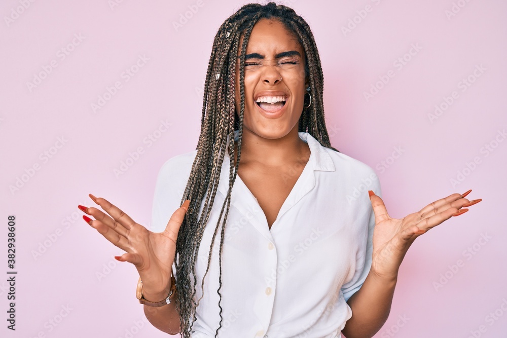 Young african american woman with braids wearing casual summer shirt celebrating mad and crazy for success with arms raised and closed eyes screaming excited. winner concept Young african american woman with braids wearing casual summer shirt celebrating mad and crazy for success with arms raised and closed eyes screaming excited. winner concept