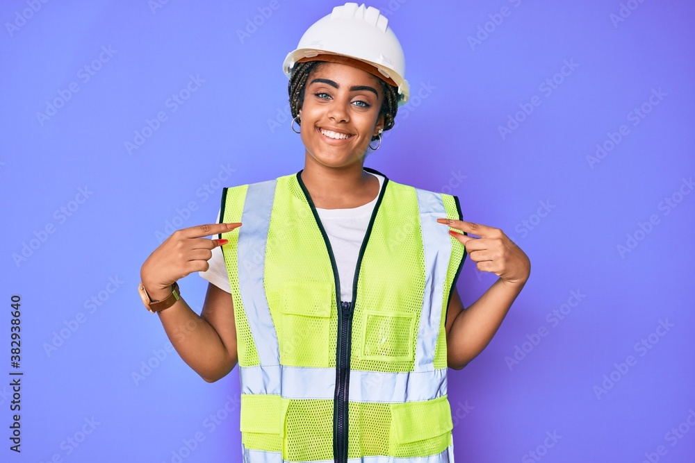 Young african american woman with braids wearing safety helmet and reflective jacket looking confident with smile on face, pointing oneself with fingers proud and happy. Young african american woman with braids wearing safety helmet and reflective jacket looking confident with smile on face, pointing oneself with fingers proud and happy.