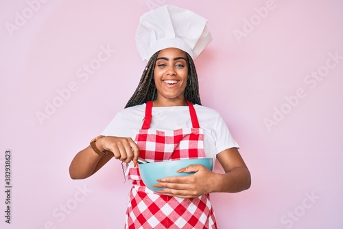 Quadro em tela Young african american woman with braids cooking using baker whisk smiling and laughing hard out loud because funny crazy joke