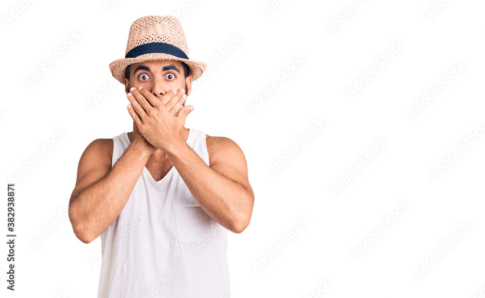 Young hispanic man wearing casual summer hat shocked covering mouth with hands for mistake. secret concept. Young hispanic man wearing casual summer hat shocked covering mouth with hands for mistake. secret concept.