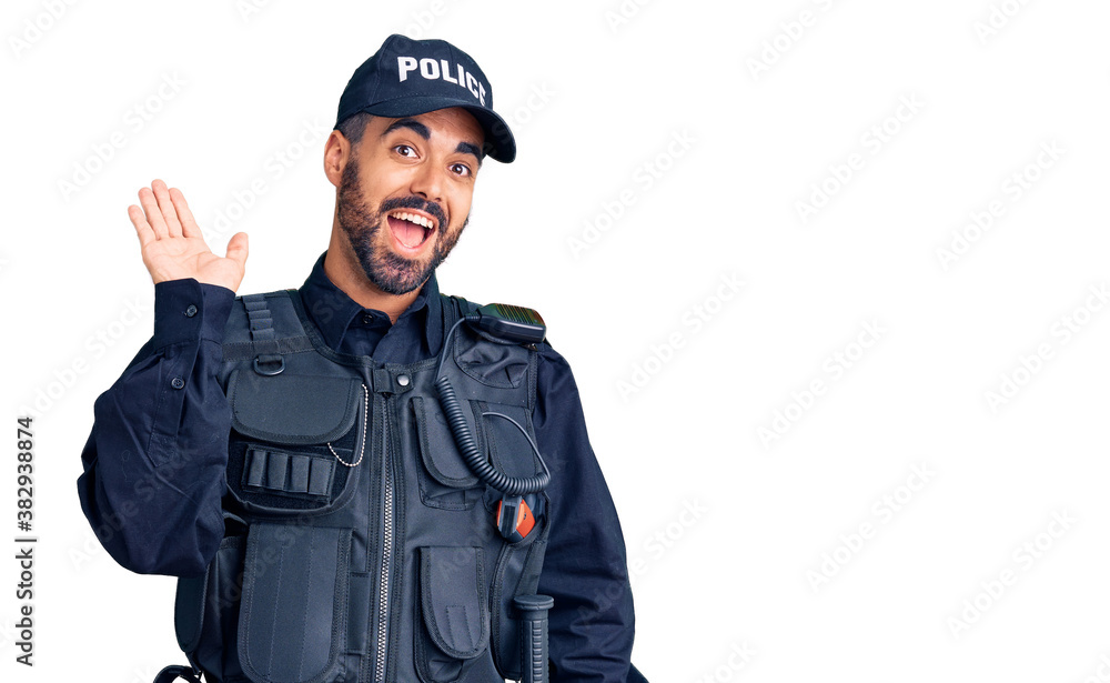 Young hispanic man wearing police uniform waiving saying hello happy and smiling, friendly welcome gesture Young hispanic man wearing police uniform waiving saying hello happy and smiling, friendly welcome gesture