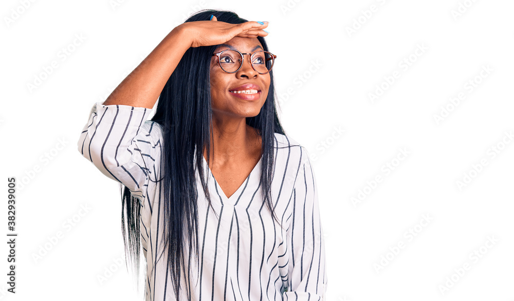 Young african american woman wearing casual clothes and glasses very happy and smiling looking far away with hand over head. searching concept. Young african american woman wearing casual clothes and glasses very happy and smiling looking far away with hand over head. searching concept.